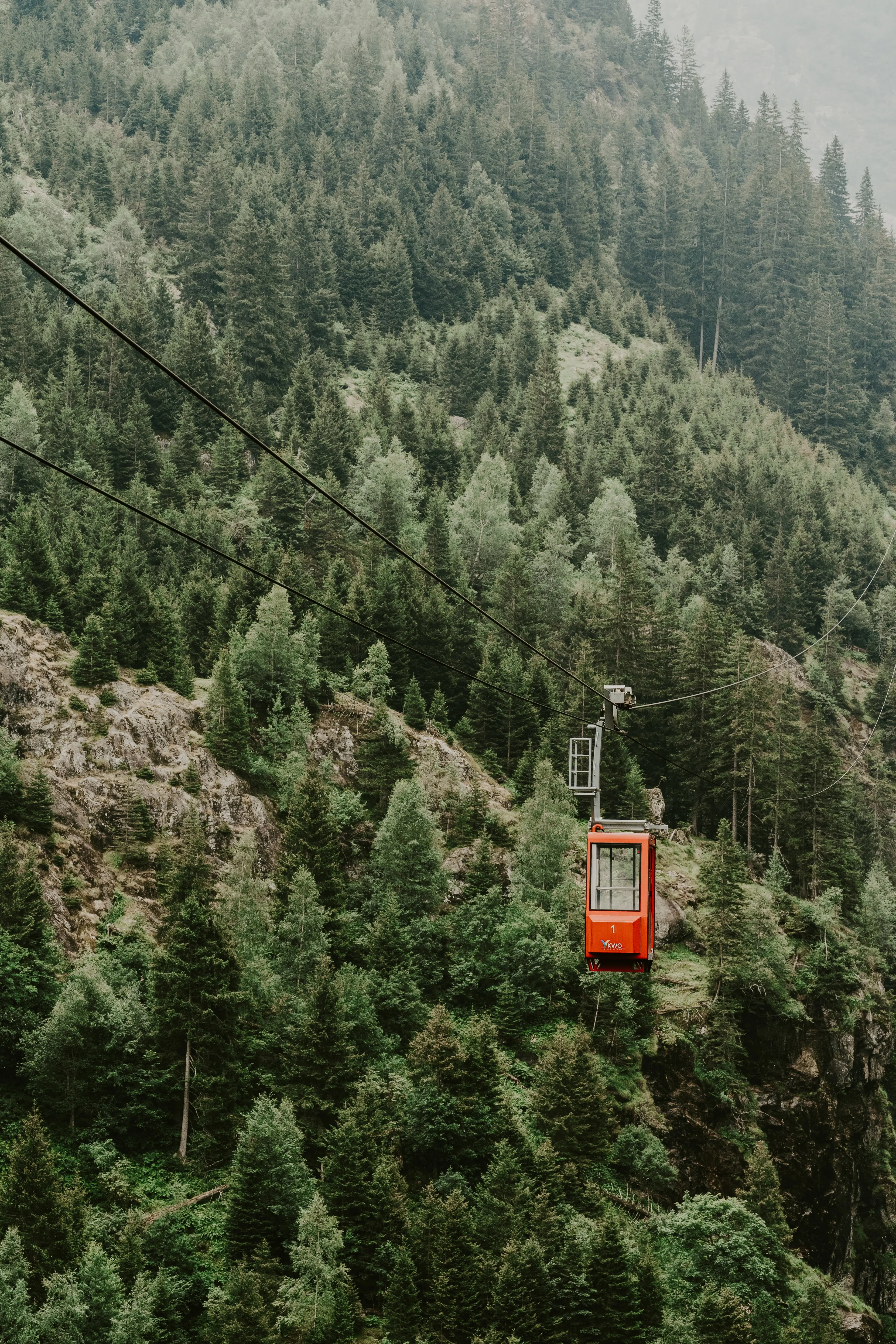 An orange chair lift suspended over a mountainous forest