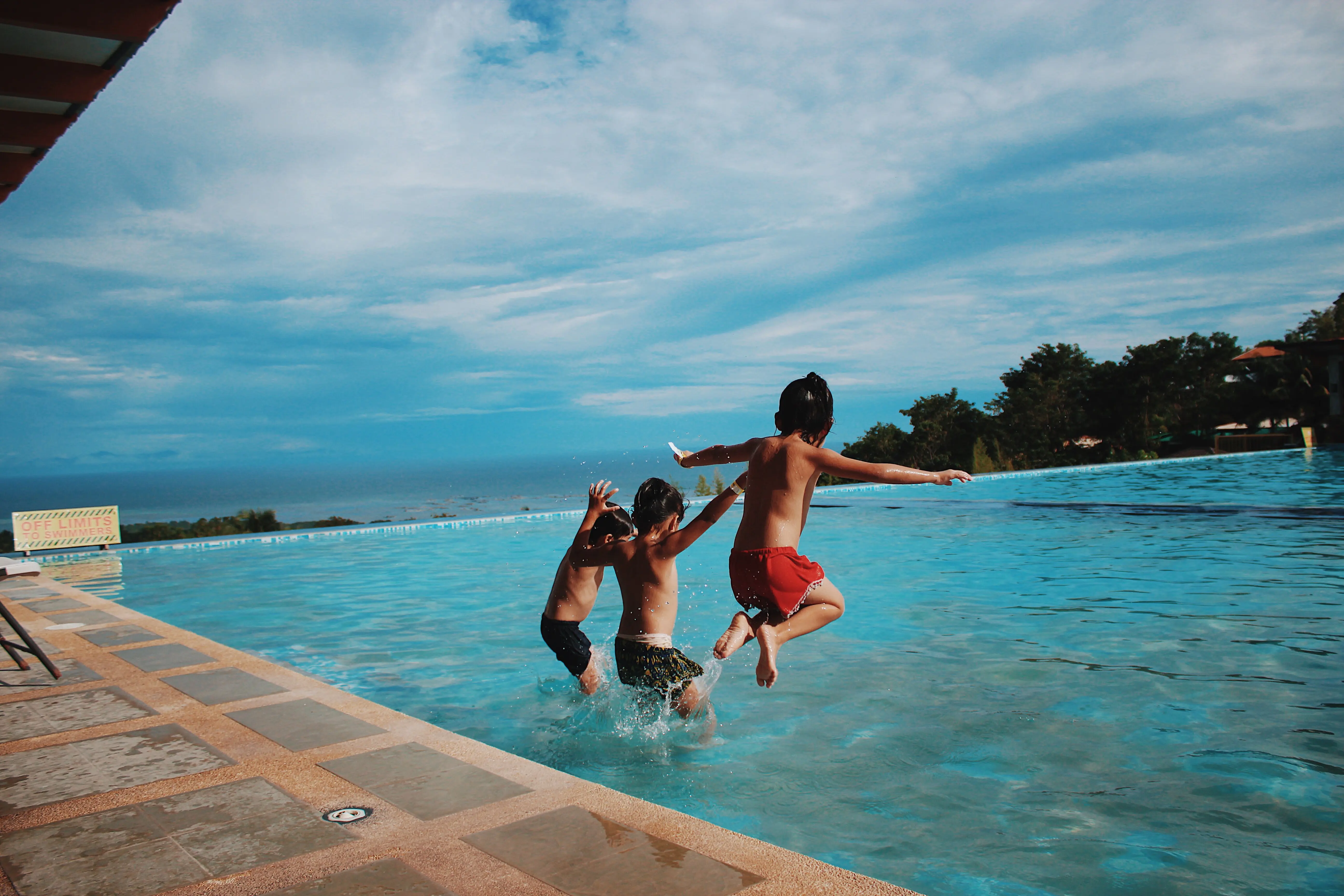 Three children jump into a swimming pool on a sunny day